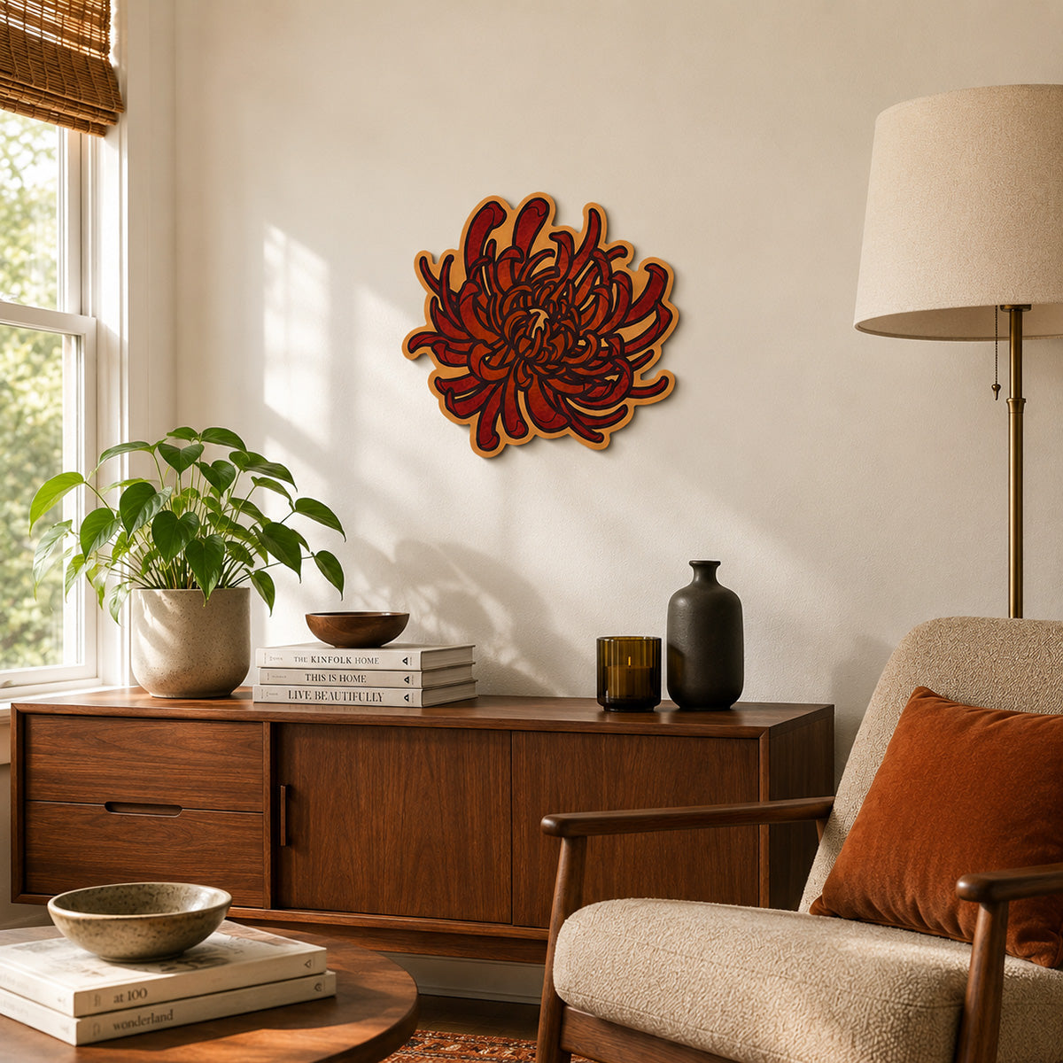 A handcrafted red chrysanthemum wood wall art piece hangs above a walnut credenza in a bright mid-century modern living room. Warm sunlight highlights the rich red petals, pastel orange accents, and contour-cut design.