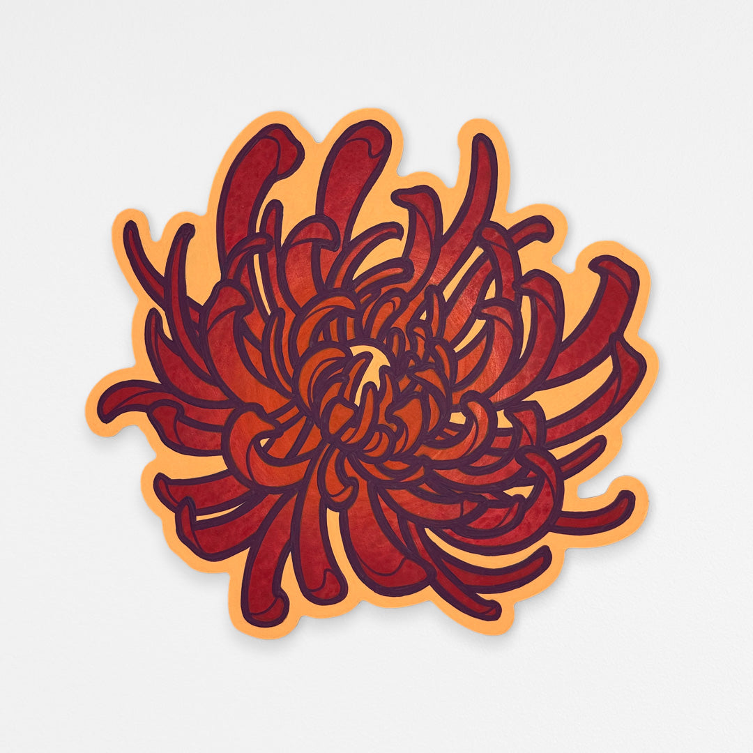 Handcrafted chrysanthemum wood wall sculpture with bright orange and coral red petals and dark purple outlines. Hanging on a white wall.