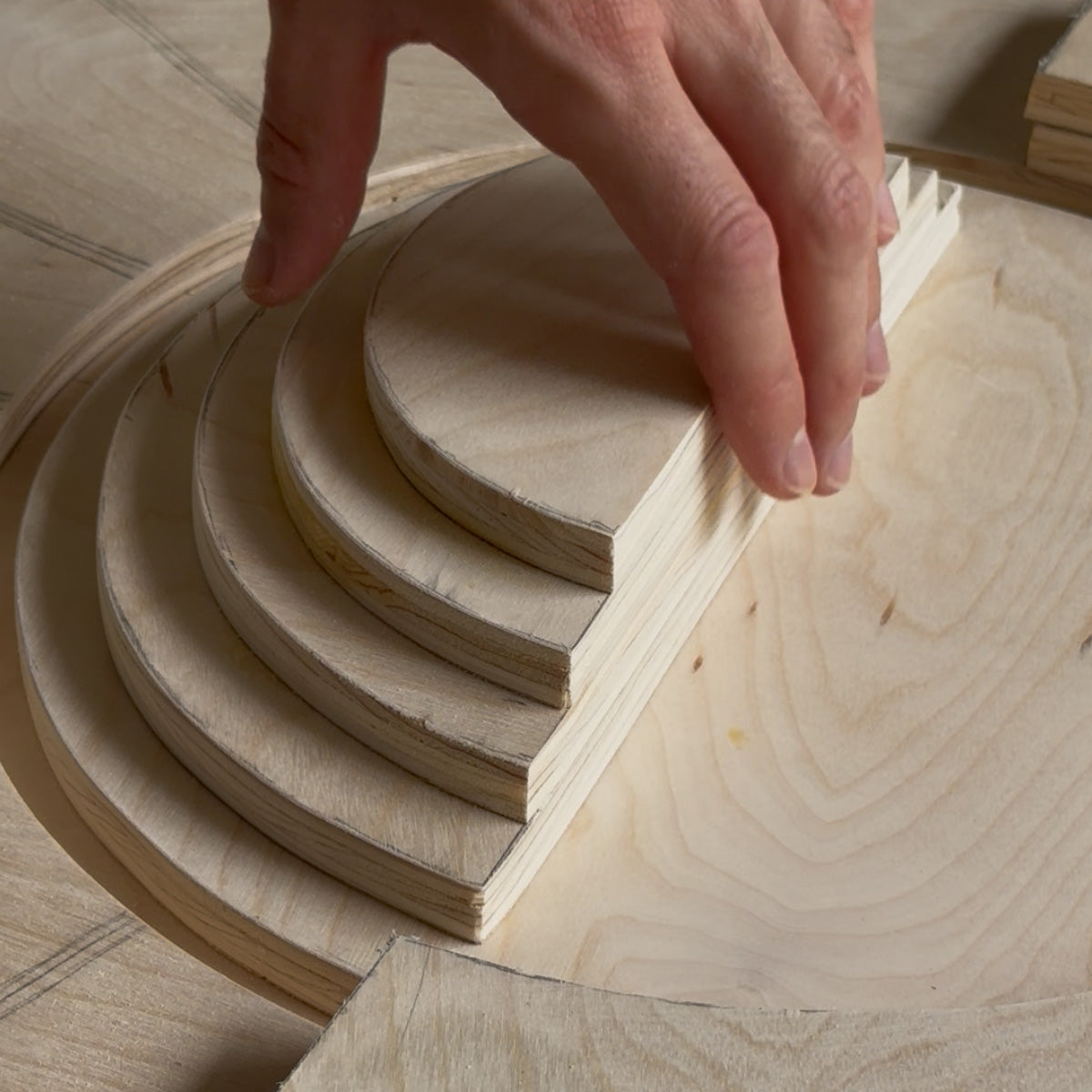 A close-up of a hand assembling light-colored wooden concentric arches on a matching wood surface.