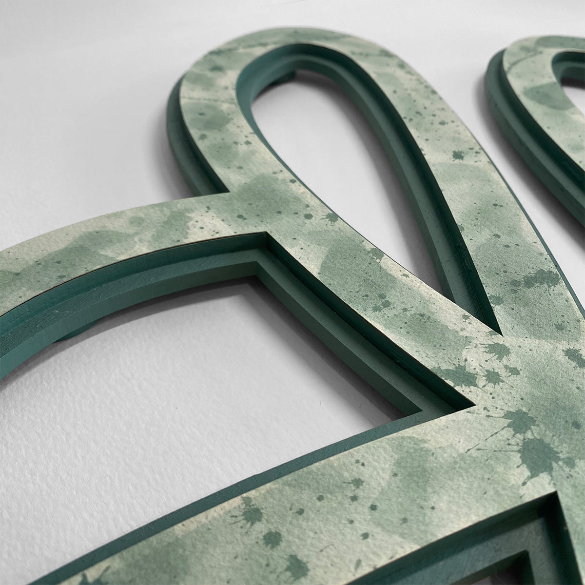 A close-up of a layered green abstract wood wall art piece with a watercolored sage green color pattern, sitting against a plain white background.