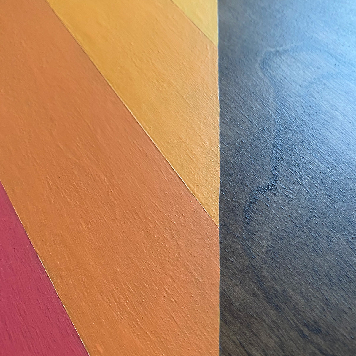 Close-up of a wood painting surface with diagonal painted color blocks in pink, orange, yellow, and walnut stained wood grain.
