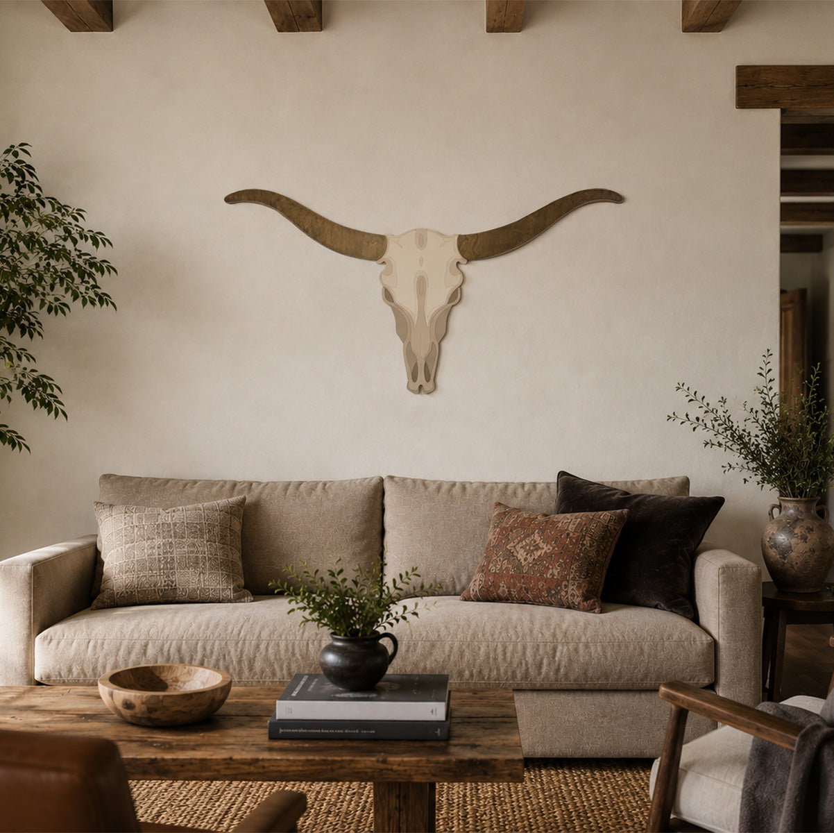 Handcrafted longhorn skull wood wall art displayed above a sofa in a modern ranch-style living room. The single-layer contour-cut design features natural wood grain horns and a painted skull, styled on a warm neutral wall with soft natural light, exposed wood beams, and rustic modern décor.