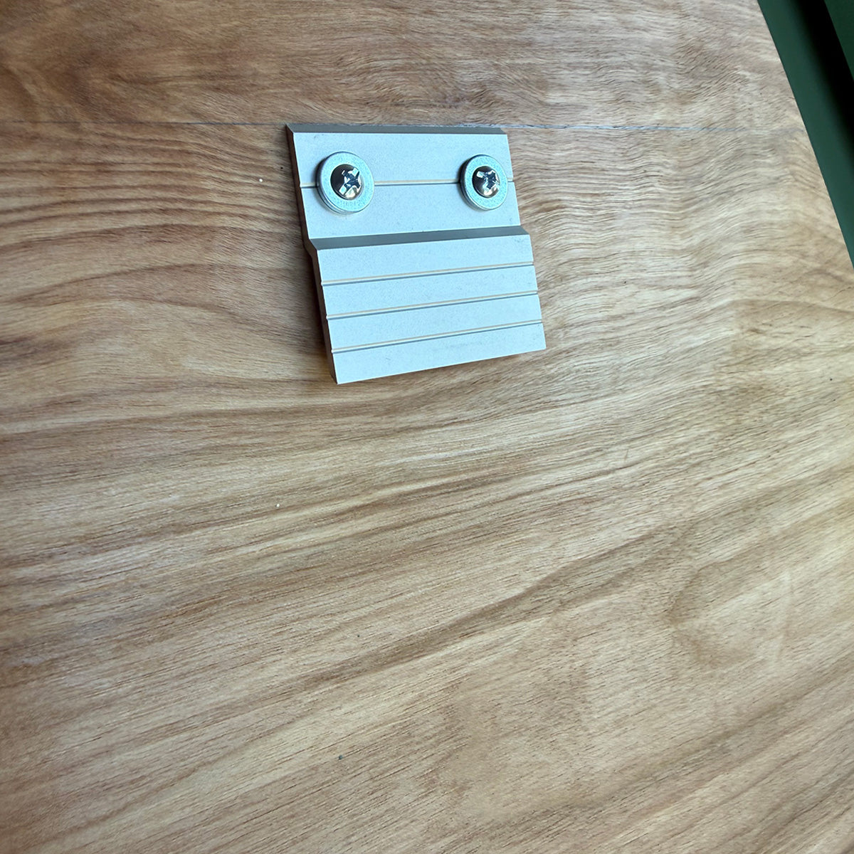 A small aluminum rear cleat with two screws, placed on a natural wood-grain surface.