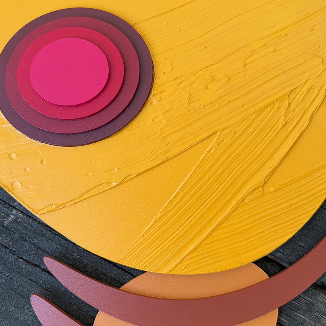 Abstract Pikachu wood wall sculpture with bright yellow texture details and red concentric circles resting on a wood tabletop.