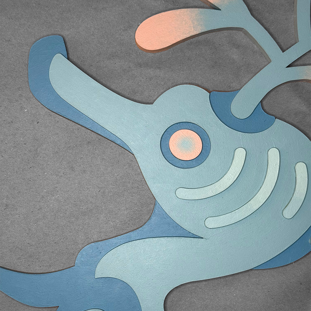 Close-up detailed photo of layered painted blue wood seadragon face with pastel pink color accents on a gray surface.