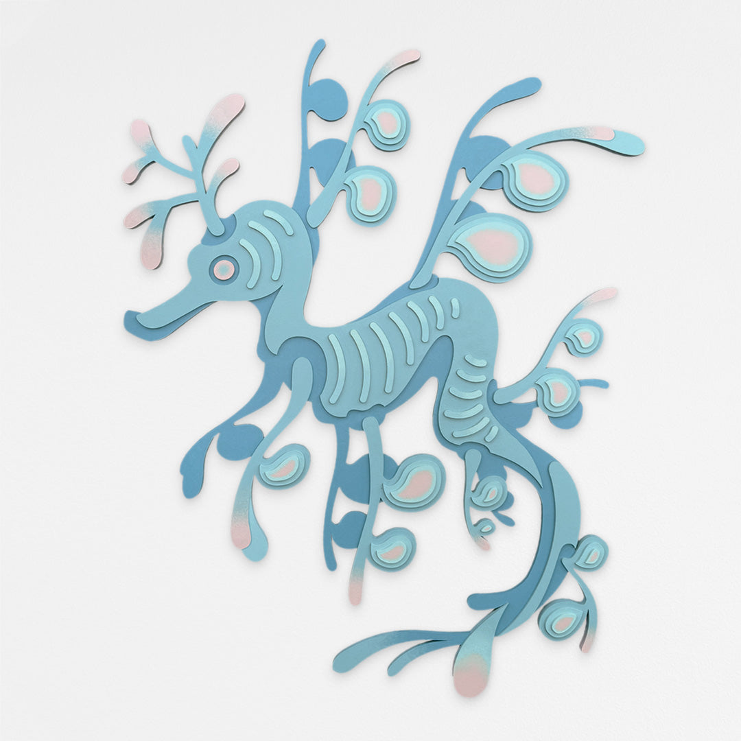 Handcrafted seadragon wood wall sculpture with layered seafoam blue and pink geometric details. Hanging on a white wall.