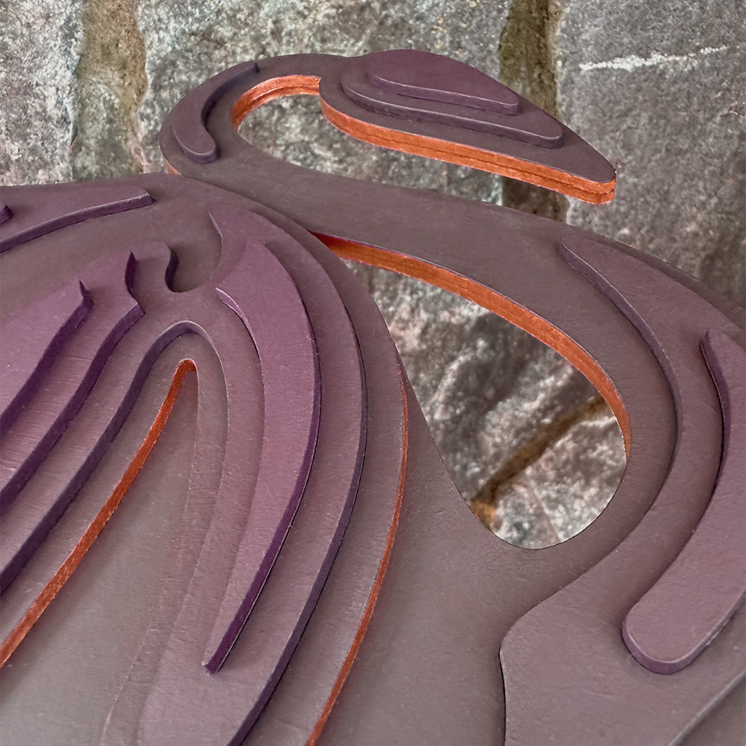 Close-up of purple layered wood wall art with a copper decorative edge against a stone wall background.