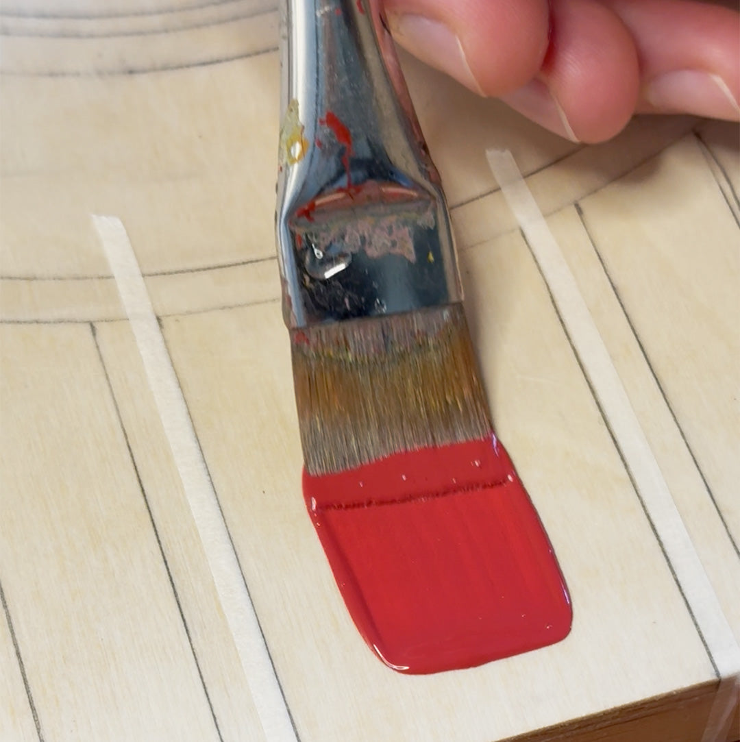 Paintbrush with red paint gliding on a wooden surface